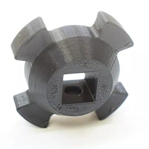 May include: A black, 3D-printed tool with a square center and four curved, wing-like protrusions. The tool has a textured surface and appears to be made of plastic. The object is set against a white background.