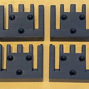 May include: Four black plastic 3D printed wall mounts with five slots each. The mounts have three screw holes on the back.