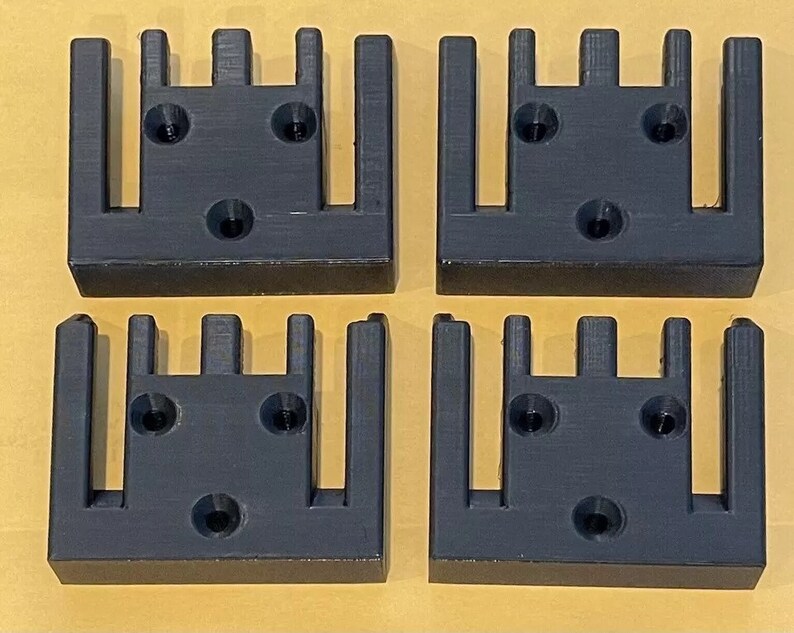 May include: Four black plastic 3D printed wall mounts with five slots each. The mounts have three screw holes on the back.
