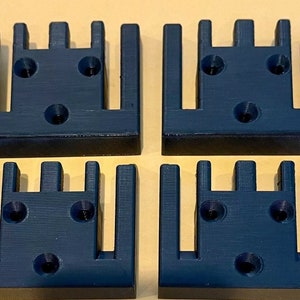 May include: Four black plastic 3D printed wall mounts with five slots each. The mounts have three screw holes on the back.
