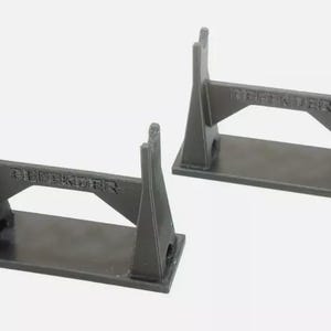 May include: Two dark gray Defender stands. Each stand has a rectangular base, two vertical supports, and a horizontal beam with the word "DEFENDER" printed on it. The stands are designed to hold an item.