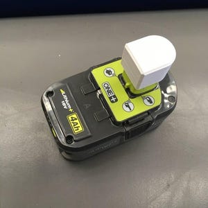 May include: A black and yellow power tool battery with a white plastic adapter on top. The battery is labeled "ONE+" and "4.0Ah 18V Lithium+ ".