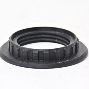 May include: A black, circular, 3D-printed object with a ridged interior and a textured exterior. The object has a wide base and a raised, threaded inner ring. The design features vertical rectangular details around the outer edge.