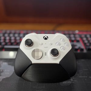 May include: A white Xbox controller with black textured grips and a silver faceplate. The controller has a standard layout with buttons, a D-pad, and analog sticks.