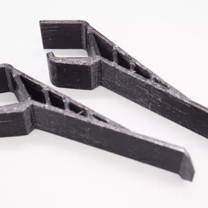 May include: Two black plastic 3D printed phone stands. The stands are designed to hold a phone upright.