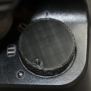 May include: Close-up of a black knob with a textured surface. The knob is part of a larger device, possibly a gaming controller or a piece of audio equipment.