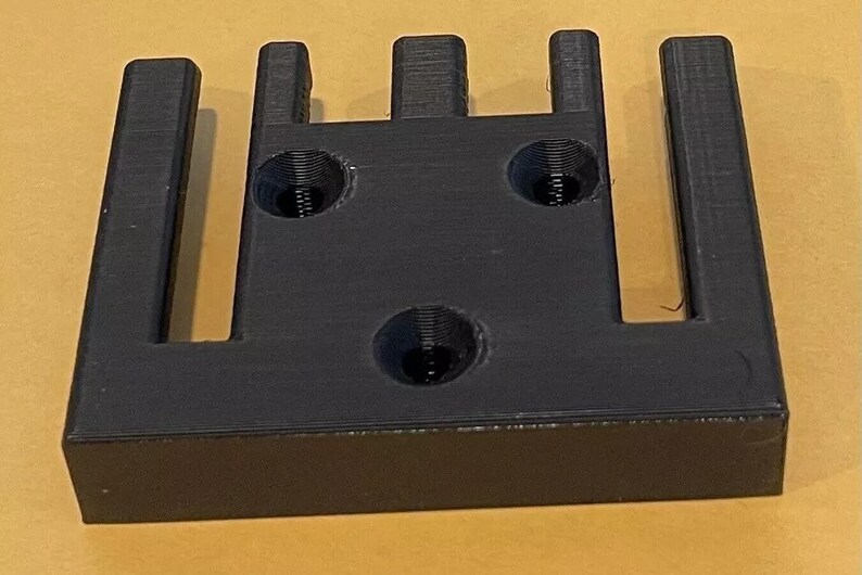 May include: A black plastic 3D printed object with five slots and three holes. The object is designed to hold multiple items.