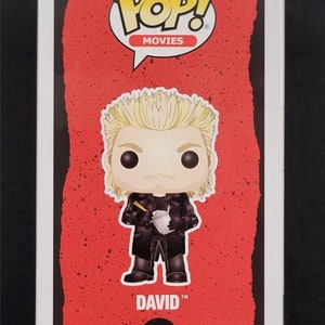 May include: Funko Pop! Movies figure of David from The Lost Boys. The figure has blonde hair and is wearing a black coat, holding a takeout container with chopsticks. The figure is on a red background with the Pop! Movies logo and the number 615.