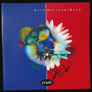 May include: Album cover for "Crash" by Dave Matthews Band. The cover is split vertically, with a blue left side and a red right side. A multi-colored, abstract design is in the center, with the band's name at the top and the word "crash" at the bottom.
