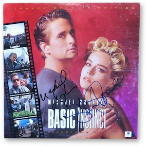 May include: A red and purple movie poster for the film "Basic Instinct" featuring Michael Douglas and Sharon Stone. The poster is signed by both actors. The poster is a special edition and includes a laserdisc, widescreen edition, director's commentary, and behind-the-scenes interviews.