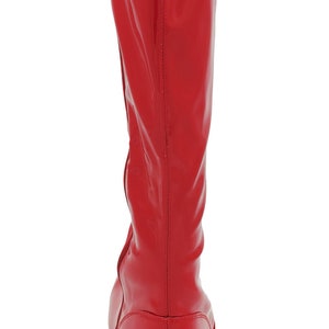 May include: Red knee-high boots with a zipper on the side and a black sole. The boots have a glossy finish and a signature on the back.