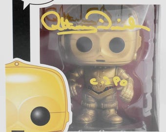 May include: A gold-colored C-3PO bobblehead figure from Star Wars, number 13 in the Pop! series, inside a clear plastic display case. The box features the Pop! logo and the Star Wars logo. The figure is signed in gold ink.