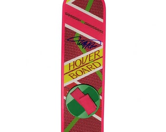 May include: A rectangular hoverboard toy with a rounded top edge, featuring a pink and red grid pattern with diagonal yellow and white stripes. The text HOVER BOARD is printed in yellow, and a blue signature is visible. A green circular footpad with a pink strap is centered.
