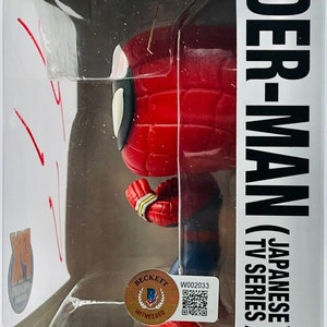 May include: A red and blue Spider-Man Pop! Vinyl figure in a box. The box has a white background with the words "Pop!" and "Marvel" in black. The figure is holding a web shooter in its right hand. The box also has a Beckett grading sticker with the number "W002033" and a QR code. The box has the text "Spider-Man (Japanese TV Series) 932" on the side.