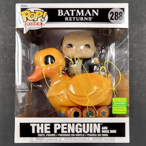 Może przedstawiać: Figurkę z winylu Funko Pop! Rides przedstawiającą Pingwina z filmu Batman Returns. Pingwin jedzie na żółtej kaczce z kółkami. Figurka jest limitowaną edycją z letniej konwencji 2022.
