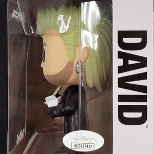 May include: A Funko Pop! Movies figure of David from the film "The Lost Boys." The figure has a stylized design with green hair, a black jacket, and is holding a white object. The box features the Pop! Movies logo and the number 615.