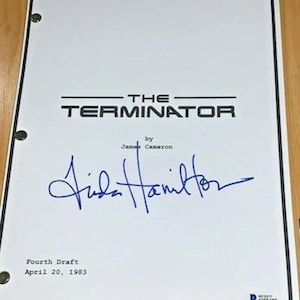 May include: A white screenplay cover for The Terminator, written by James Cameron, dated April 20, 1983. The document features a blue ink signature by Linda Hamilton, three metal binding holes on the left side, and a small authentication sticker.