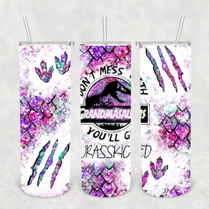 Może przedstawiać: Biały kubek z akwarelowym wzorem w kolorze różowym, fioletowym i zielonym. Kubek ma grafikę dinozaura z tekstem "Don't mess with Grandmasaurus you'll get Jurassic'd".