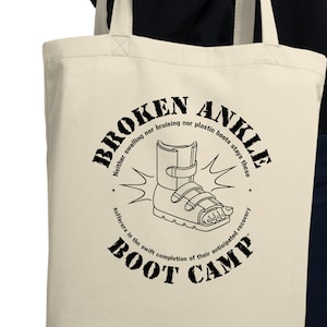 May include: A white canvas tote bag with black text and a graphic of a broken ankle boot. The text reads "Broken Ankle Boot Camp" and "Heals swelling on bruising near plastic boots stay there, suffers in the swift completion of their anticipated recovery."