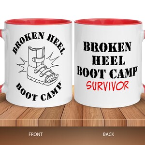 May include: White ceramic coffee mug with a red rim. The front of the mug has a black and white illustration of a broken foot in a boot with the text "Broken Heel Boot Camp". The back of the mug has the text "Broken Heel Boot Camp Survivor" in black with the word "Survivor" in red.