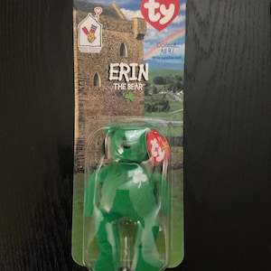 May include: Green plush bear with a shamrock on its chest. The bear is packaged in a plastic case with a Ty tag and a background image of a castle. The packaging also includes the text "Erin the Bear" and "Collect All 4!"