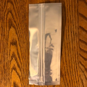May include: A clear plastic stand-up pouch with a zipper closure. The pouch is made of a shiny, metallic material.