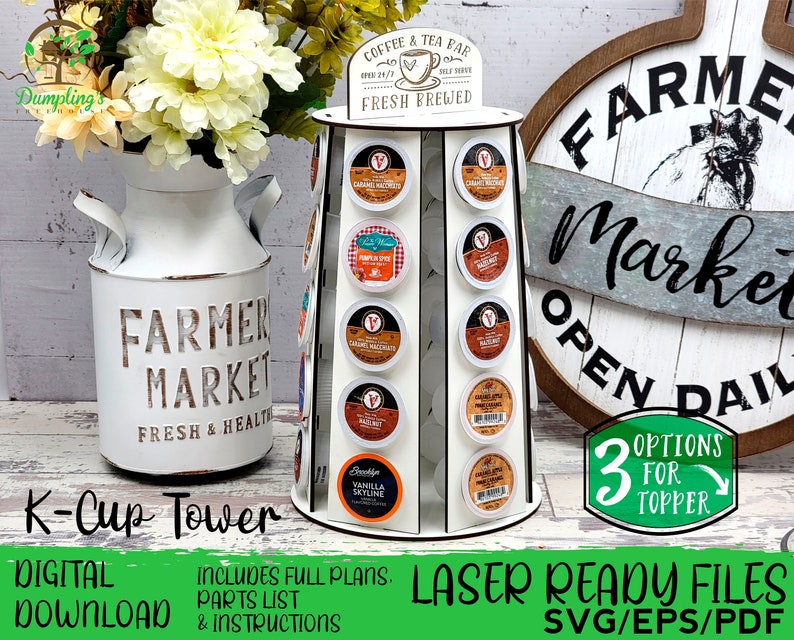 K&ouml;nnte beinhalten: Ein wei&szlig;er K-Cup-Kaffeepad-Turm mit mehreren Schlitzen, der verschiedene Kaffeepads enth&auml;lt. Der Turm hat ein Schild mit der Aufschrift "Coffee & Tea Bar, Fresh Brewed". Das Bild enth&auml;lt auch eine wei&szlig;e Vase im Bauernhausstil mit Blumen und ein Holzschild mit der Aufschrift "Farmer Market".