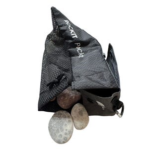 May include: A black Rockit Pocket bag with a mesh front and a diamond pattern on the back. The bag is open, revealing several smooth, gray and brown stones. The text "ROCKIT POCKET" is printed on the bag.