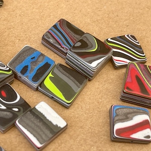 May include: A collection of colourful square-shaped resin tiles with swirling patterns in shades of black, white, red, blue, green, and yellow.