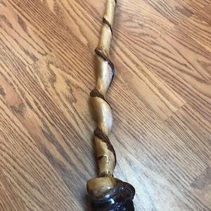 May include: A wooden walking stick with a twisted, spiral design. The stick is brown and has a dark brown knob at the bottom.