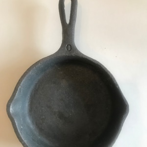 May include: A black cast iron skillet with a single handle. The skillet has a smooth, dark surface and a small, round indentation on the handle.