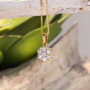 Op de afbeelding: Een gouden ketting met een bloemvormige hanger met meerdere heldere edelstenen. De ketting hangt aan een verweerde, lichtgekleurde houten tak, met een vage groene plant op de achtergrond.