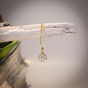 Op de afbeelding: Een gouden hangerketting met een bloemvormig ontwerp met meerdere heldere edelstenen. De hanger hangt aan een fijne gouden ketting. De ketting wordt gepresenteerd tegen een neutrale achtergrond.