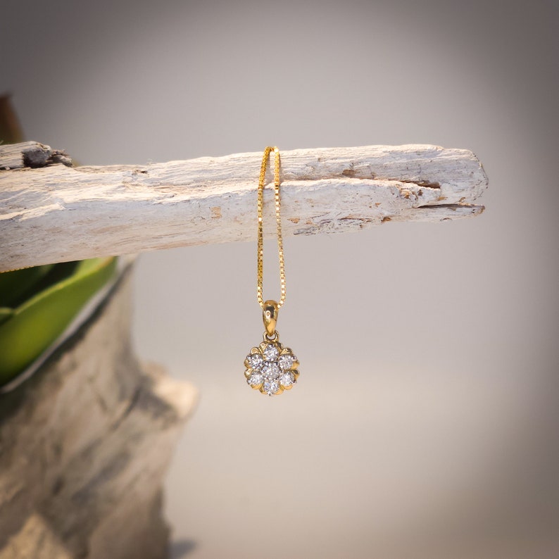 Op de afbeelding: Een gouden hangerketting met een bloemvormig ontwerp met meerdere heldere edelstenen. De hanger hangt aan een fijne gouden ketting. De ketting wordt gepresenteerd tegen een neutrale achtergrond.