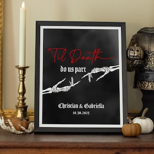 May include: A framed black and white print with the text "Til Death do us part" in red script. The image features skeleton hands reaching towards each other. The names "Christian & Gabriella" and the date "10.30.2025" are also displayed.