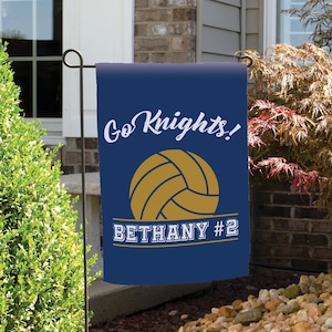 Peut inclure: Un drapeau de jardin bleu avec un ballon de volley-ball doré et le texte "Go Knights! Bethany #2".