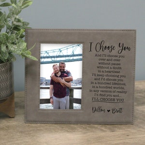 May include: A gray picture frame with a photo of two people hugging in front of a bridge. The frame has a quote that reads "I Choose You" and "And I'll choose you over and over without pause without a doubt in a heartbeat I'll keep choosing you and I'd choose you in a hundred lifetimes, in a hundred worlds, in any version of reality I'd find you and... I'LL CHOOSE YOU" with the names Dillon and Brett at the bottom.