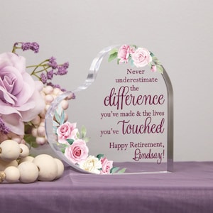 May include: A clear heart-shaped acrylic paperweight with a floral design and the text "Never underestimate the difference you've made & the lives you've touched. Happy Retirement, Lindsay!"