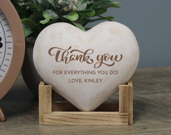 May include: White heart-shaped stone with the text "Thank you for everything you do! Love, Kinley" in brown lettering. The stone is sitting in a wooden stand.