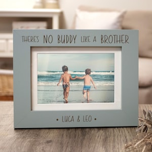 May include: A light blue wooden picture frame with the text "There's no buddy like a brother" and "Luca & Leo" printed on it. The frame holds a photo of two boys walking on a beach.