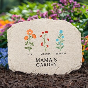 May include: A beige stone garden marker with the text "MAMA'S GARDEN" and three floral illustrations. The flowers are orange, red, and blue, with the names "JACK", "MIRANDA", and "BRANDON" below each.