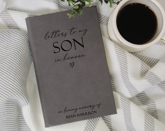 Puede incluir: Diario gris con el texto "letters to my son in heaven" y un símbolo de corazón. El diario también tiene el texto "in loving memory of RYAN HARRISON" impreso en la parte inferior.