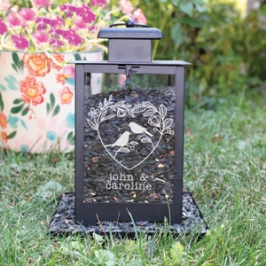 May include: Black metal bird feeder with a glass front featuring a heart design with two birds and the text "john & caroline".