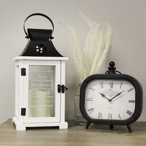 May include: White lantern with a black metal top and a glass pane with the text "Never underestimate the difference you've made and the lives you've touched. Happy Retirement, Marie!"  A black clock with Roman numerals and the text "Antique 1850" is in the background.