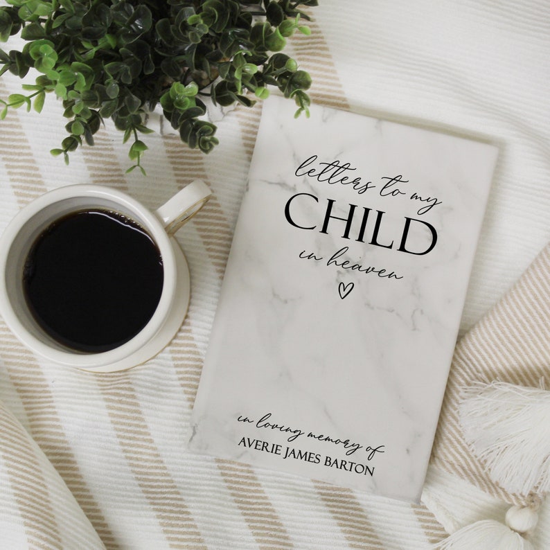 May include: A white marble-patterned journal with the text "letters to my CHILD in heaven" and a small heart symbol. The journal is for writing letters to a child who has passed away. The text "in loving memory of AVERIE JAMES BARTON" is printed at the bottom of the journal.