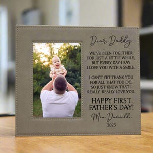 First Father's Day Picture Frame with "Dear Daddy" Poem and personalized with baby's name in tan sitting on a table inside a home