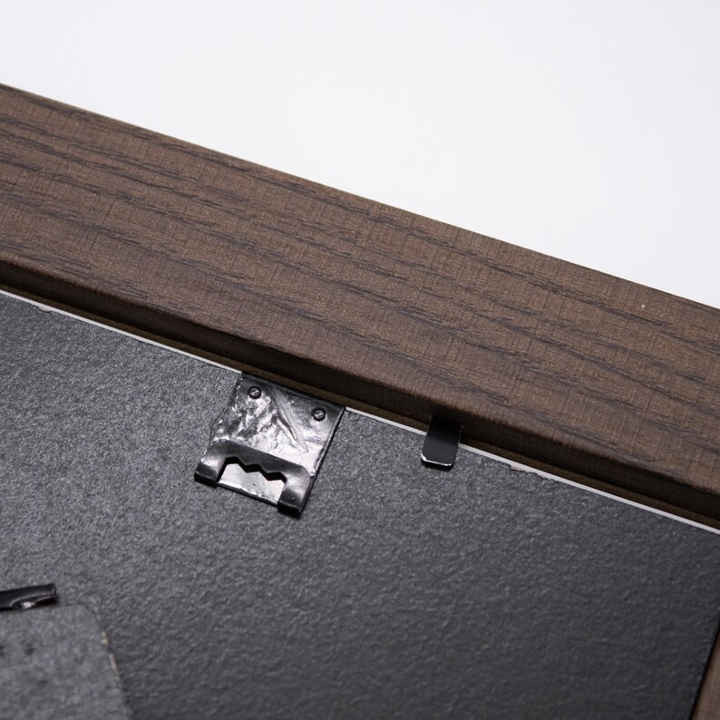 May include: Close-up of a brown wooden picture frame with two metal hanging clips attached to the back.