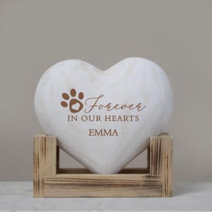May include: White heart-shaped stone with a paw print and the text "Forever in our hearts Emma". The stone is on a wooden stand.