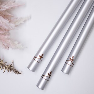 May include: Three silver wind chimes with a leaf design hanging from a white background.