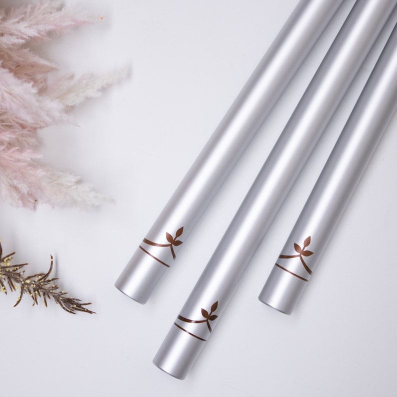 May include: Three silver wind chimes with a leaf design hanging from a white background.